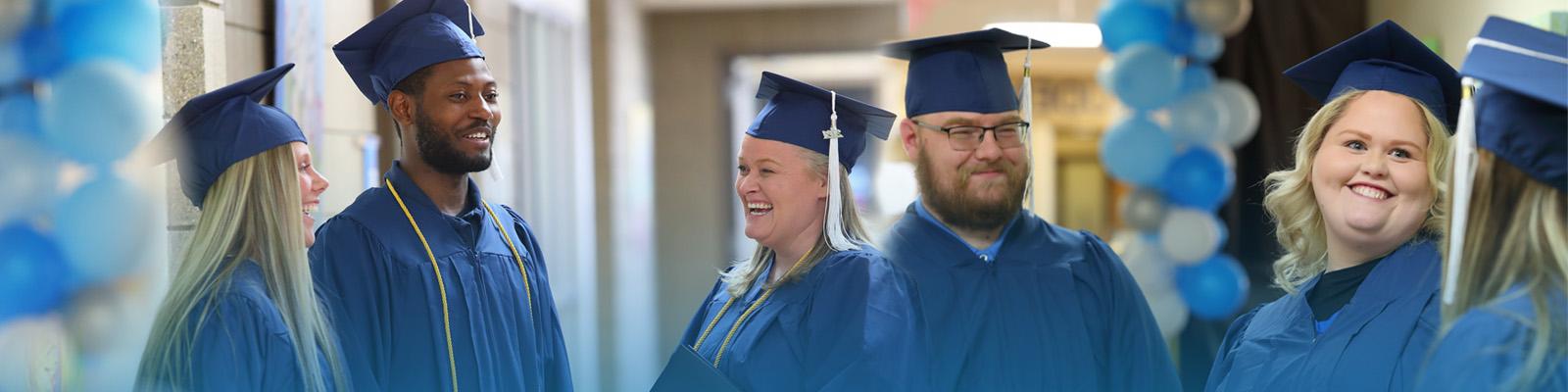 graduates smiling in hallway with blue toned balloons